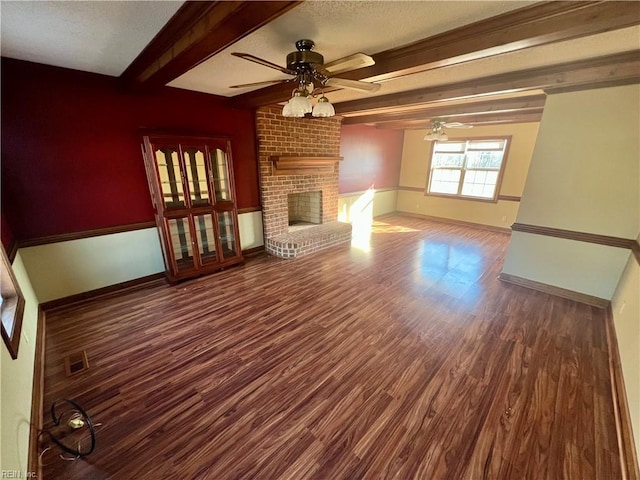 unfurnished living room with ceiling fan, dark wood-type flooring, visible vents, a brick fireplace, and beam ceiling