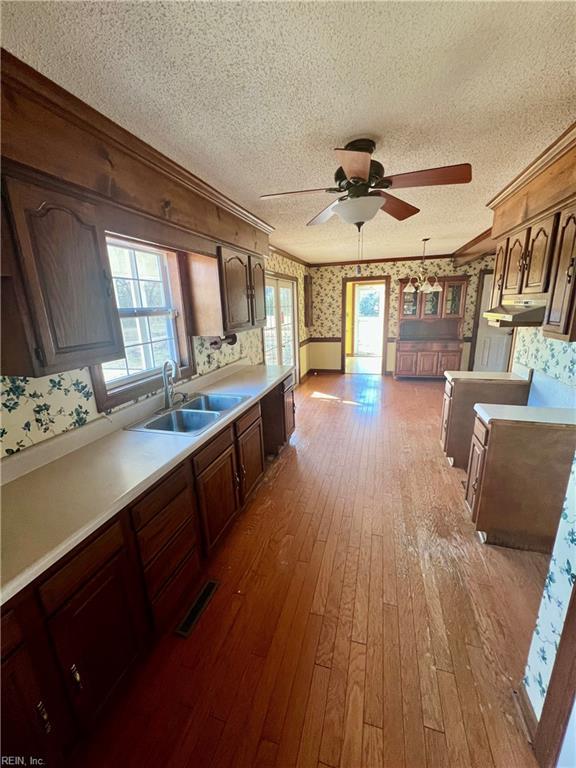 kitchen with light countertops, ornamental molding, a sink, a textured ceiling, and wallpapered walls