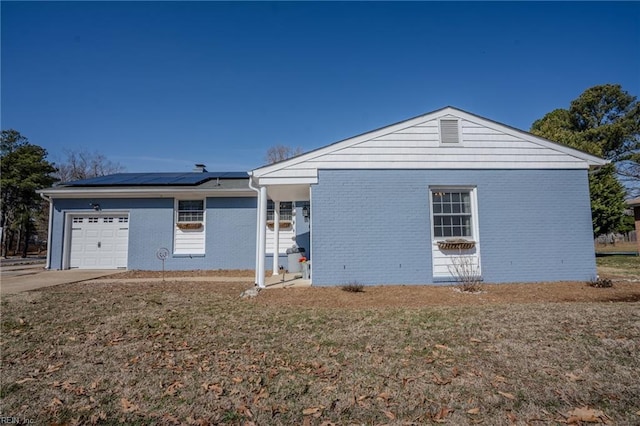 view of front facade with an attached garage, solar panels, brick siding, concrete driveway, and a front yard