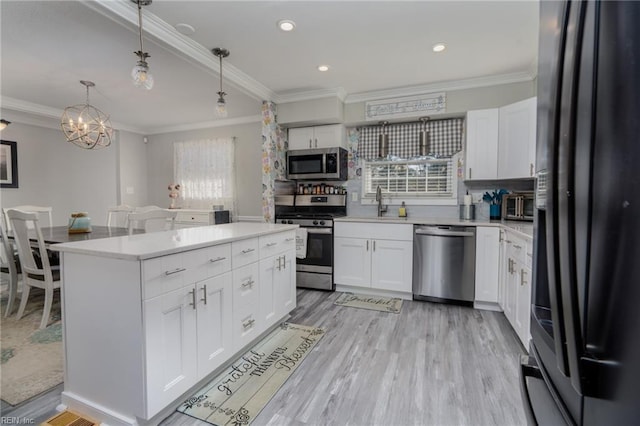 kitchen with stainless steel appliances, ornamental molding, light countertops, and light wood-style flooring