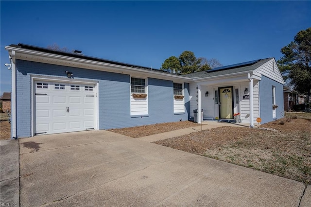 ranch-style house with concrete driveway, brick siding, an attached garage, and solar panels