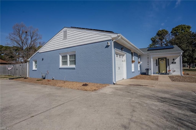 view of front of house with a garage, brick siding, fence, concrete driveway, and roof mounted solar panels