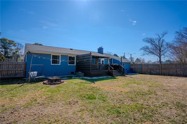 rear view of house with an outdoor fire pit, a fenced backyard, a lawn, and a deck