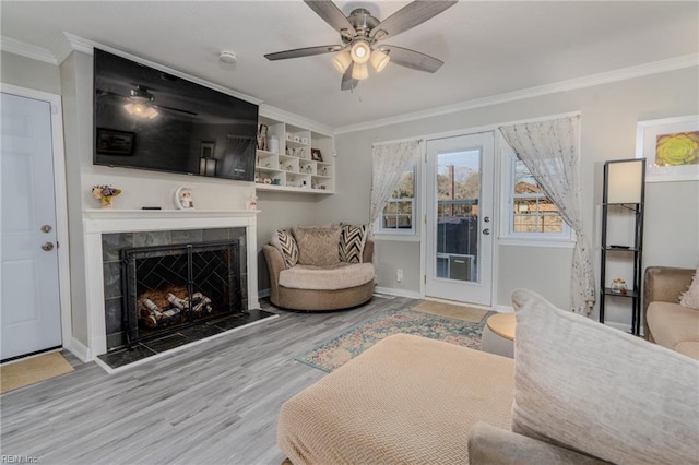 living room with ceiling fan, a tile fireplace, wood finished floors, baseboards, and ornamental molding