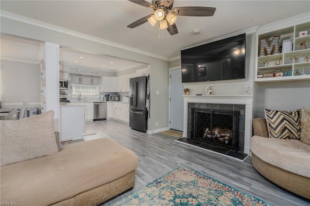 living area featuring a fireplace, ornamental molding, light wood-style floors, ceiling fan, and baseboards