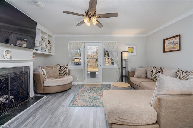 living room with baseboards, a ceiling fan, wood finished floors, crown molding, and a fireplace