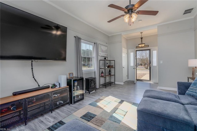 living area with a wood stove, visible vents, wood finished floors, and ornamental molding