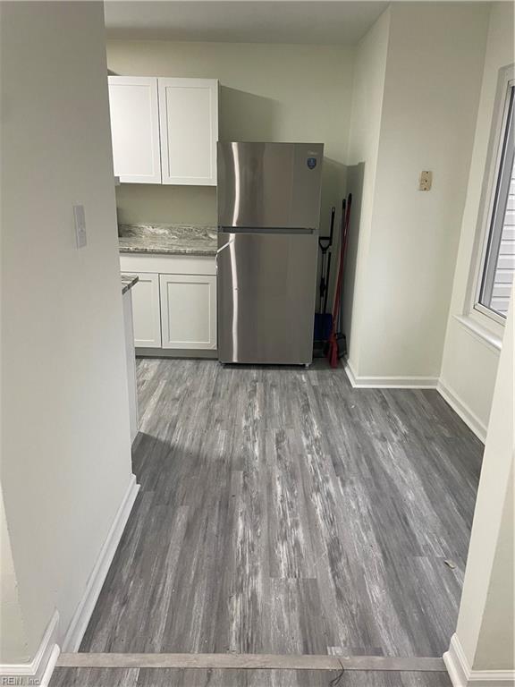 kitchen with dark wood-type flooring, freestanding refrigerator, white cabinetry, light stone countertops, and baseboards