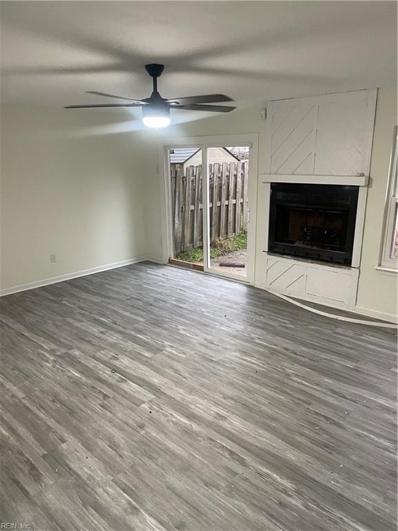 unfurnished living room with baseboards, a fireplace, a ceiling fan, and wood finished floors