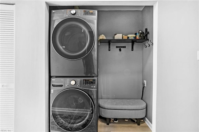 clothes washing area with stacked washer / dryer, laundry area, baseboards, and wood finished floors