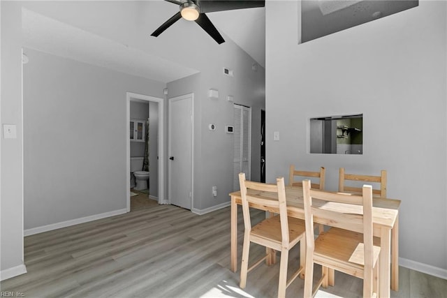 dining area featuring a towering ceiling, baseboards, a ceiling fan, and wood finished floors