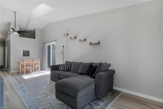 living room with vaulted ceiling with skylight, wood finished floors, a ceiling fan, and baseboards