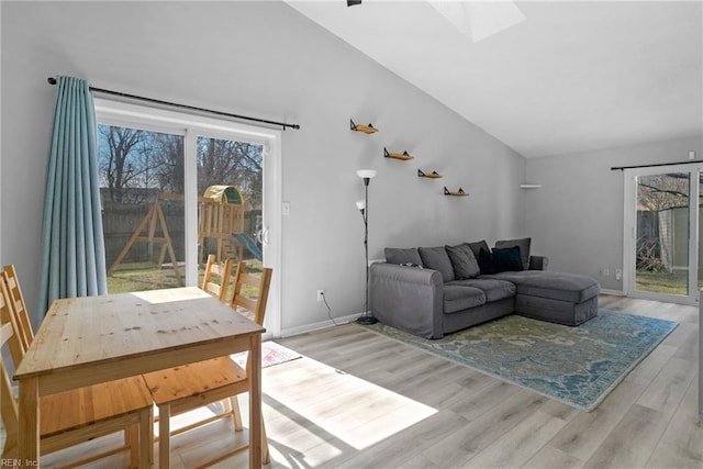 living area featuring light wood-type flooring, vaulted ceiling with skylight, and baseboards