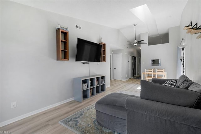 living area with light wood finished floors, visible vents, ceiling fan, vaulted ceiling with skylight, and baseboards