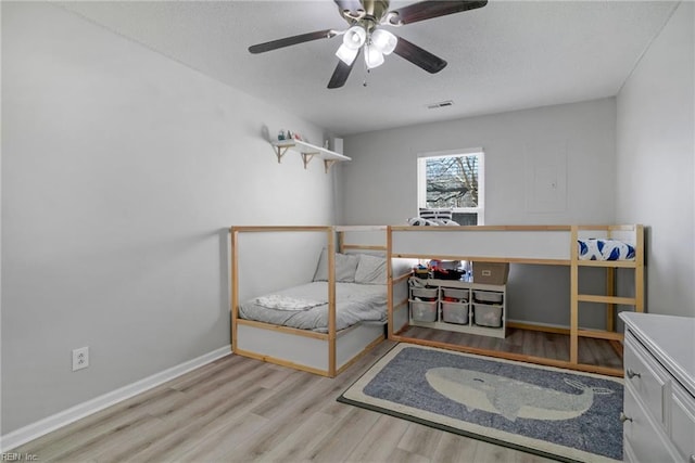 bedroom with a ceiling fan, visible vents, baseboards, and wood finished floors