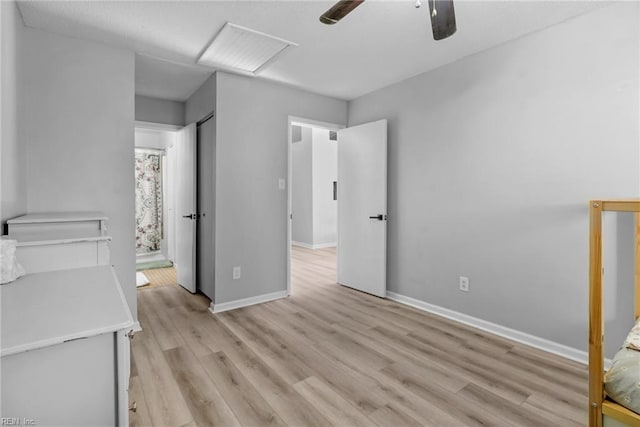 unfurnished bedroom featuring light wood finished floors, attic access, baseboards, a ceiling fan, and ensuite bath