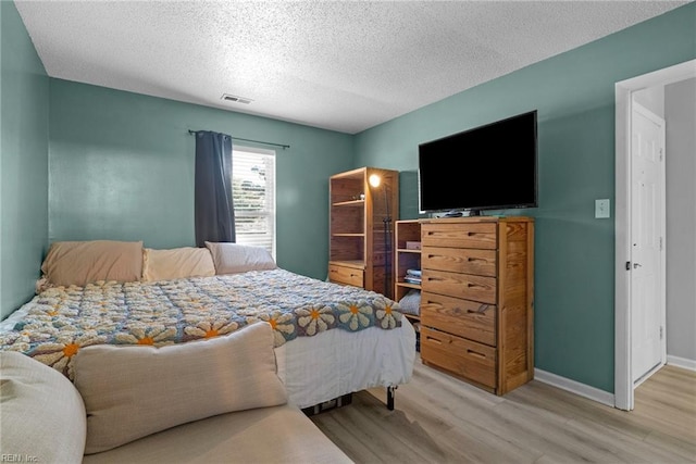 bedroom with a textured ceiling, light wood-type flooring, visible vents, and baseboards