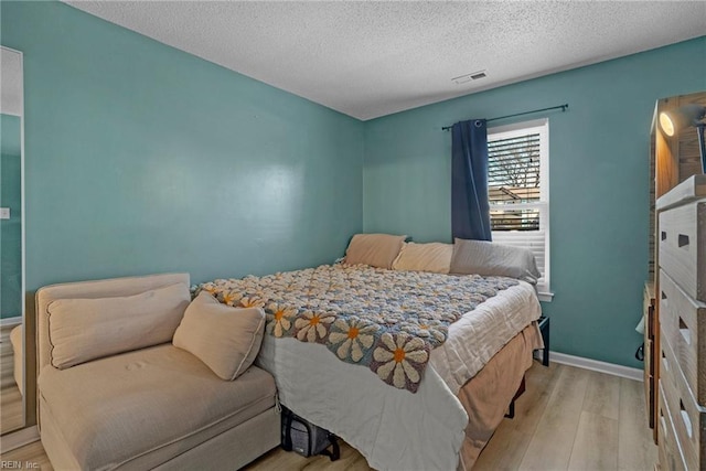 bedroom featuring a textured ceiling, wood finished floors, visible vents, and baseboards