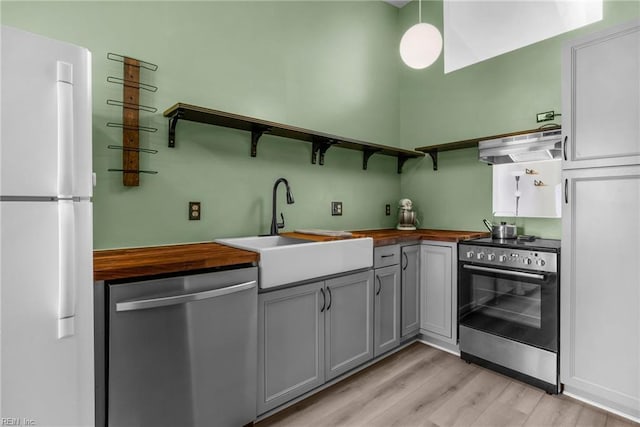 kitchen featuring under cabinet range hood, butcher block counters, appliances with stainless steel finishes, and open shelves