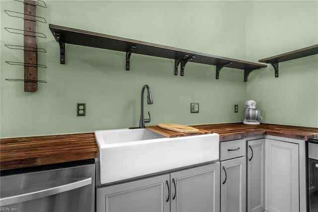 kitchen with a sink, open shelves, stainless steel dishwasher, and wood counters