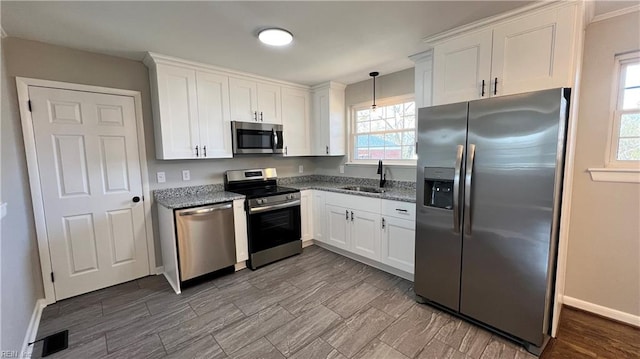 kitchen with hanging light fixtures, appliances with stainless steel finishes, white cabinetry, a sink, and dark stone countertops