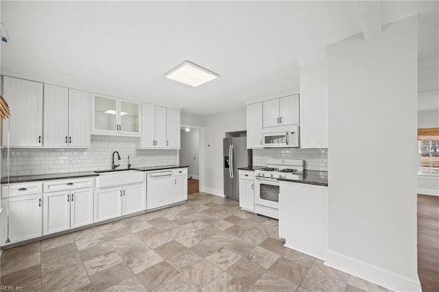 kitchen with white appliances, a sink, white cabinets, tasteful backsplash, and dark countertops