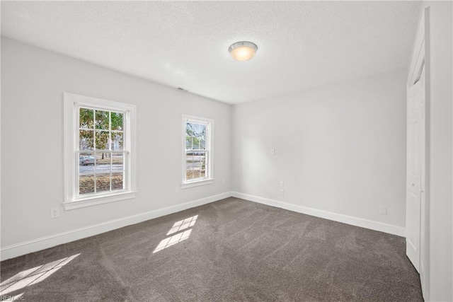 empty room with dark colored carpet, a textured ceiling, and baseboards