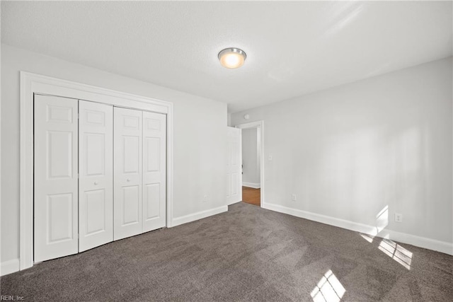 unfurnished bedroom with baseboards, dark colored carpet, and a closet