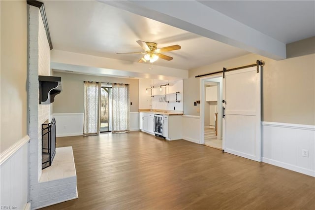 unfurnished living room with wainscoting, a barn door, wine cooler, and a brick fireplace