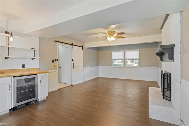 kitchen with a barn door, beverage cooler, a fireplace, white cabinets, and wainscoting