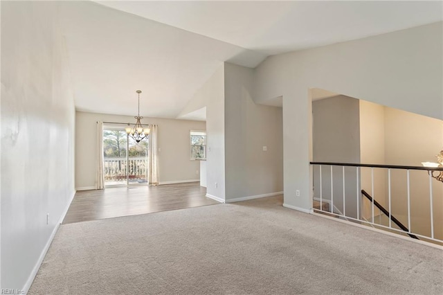 carpeted empty room featuring baseboards, a chandelier, and vaulted ceiling