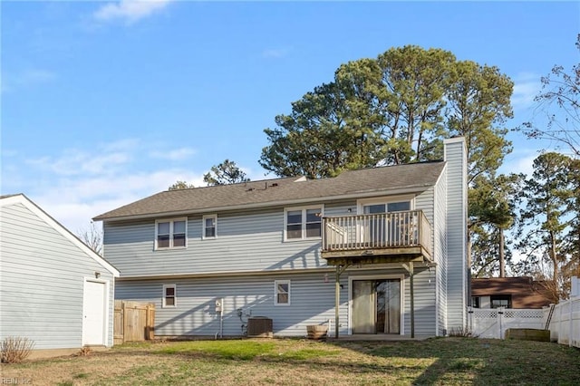 rear view of property with a balcony, a chimney, fence, a yard, and central AC