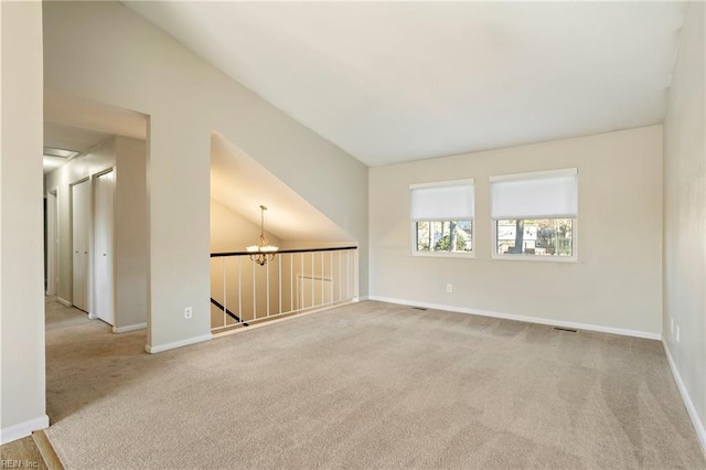 empty room featuring a chandelier, light colored carpet, and baseboards