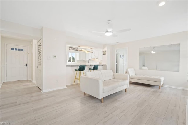 living room featuring baseboards, ceiling fan, and light wood finished floors