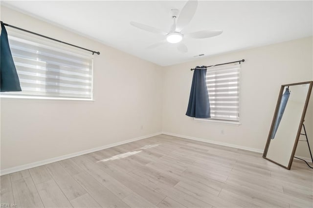 spare room with light wood-style floors, ceiling fan, visible vents, and baseboards