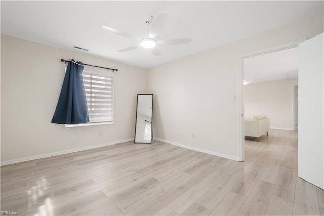 spare room featuring light wood finished floors, ceiling fan, visible vents, and baseboards