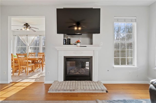 living area with a wealth of natural light, a glass covered fireplace, baseboards, and wood finished floors