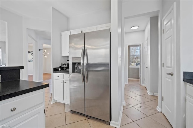 kitchen with dark countertops, light tile patterned floors, stainless steel fridge, and white cabinets