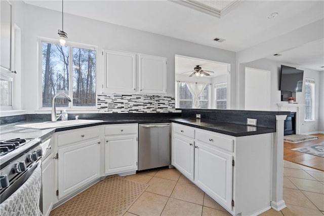 kitchen featuring light tile patterned floors, dishwasher, dark countertops, a peninsula, and a sink