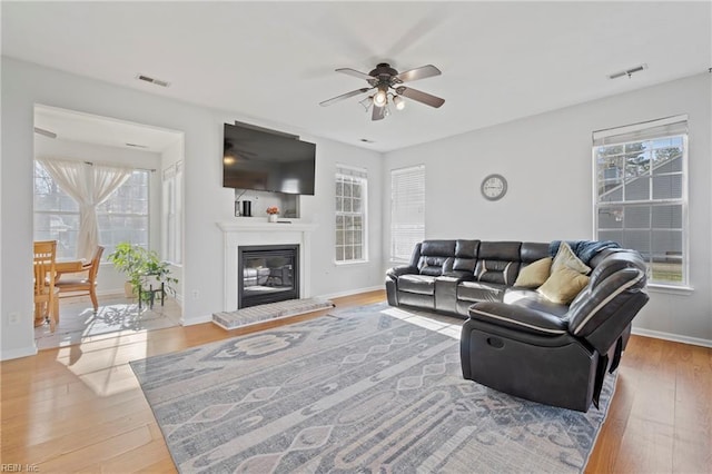 living area featuring wood-type flooring, a glass covered fireplace, visible vents, and baseboards