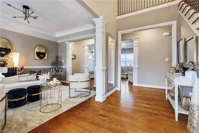 living area featuring baseboards, wood-type flooring, ornamental molding, stairs, and ornate columns