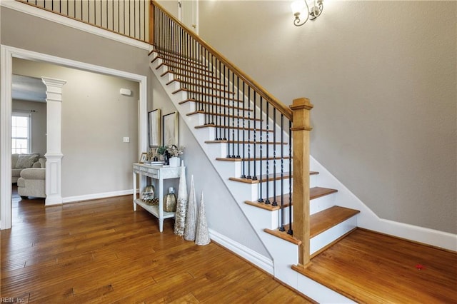 stairs featuring a towering ceiling, ornate columns, wood-type flooring, and baseboards