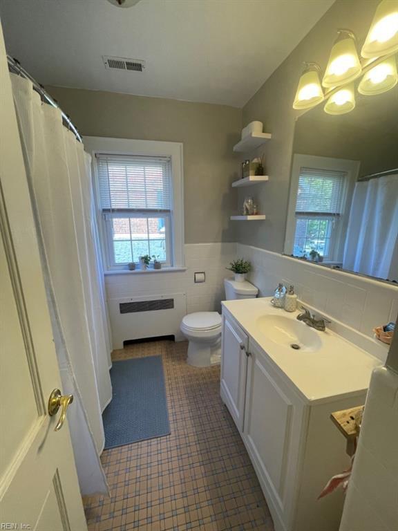 full bath with a wainscoted wall, vanity, visible vents, tile walls, and radiator heating unit