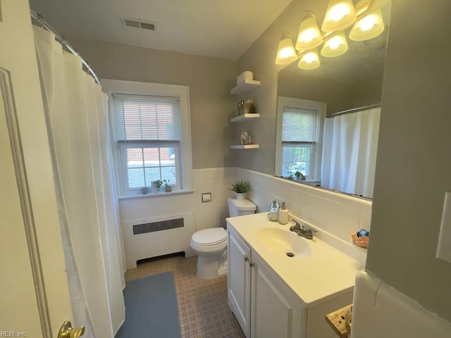 bathroom with visible vents, toilet, radiator heating unit, vanity, and tile walls