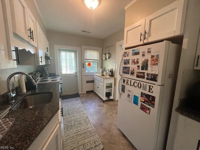 kitchen with freestanding refrigerator, white cabinetry, a sink, dark stone countertops, and range