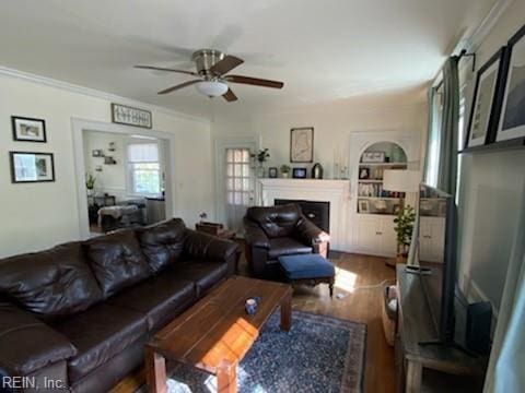 living area with a fireplace, wood finished floors, a ceiling fan, built in features, and crown molding