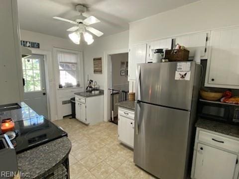 kitchen with black microwave, dark countertops, freestanding refrigerator, and white cabinets