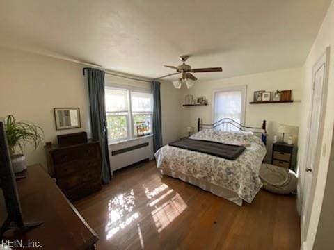 bedroom featuring ceiling fan, a baseboard heating unit, and wood finished floors