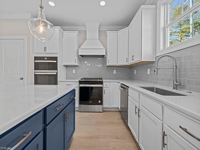 kitchen with blue cabinetry, stainless steel appliances, light countertops, custom range hood, and a sink