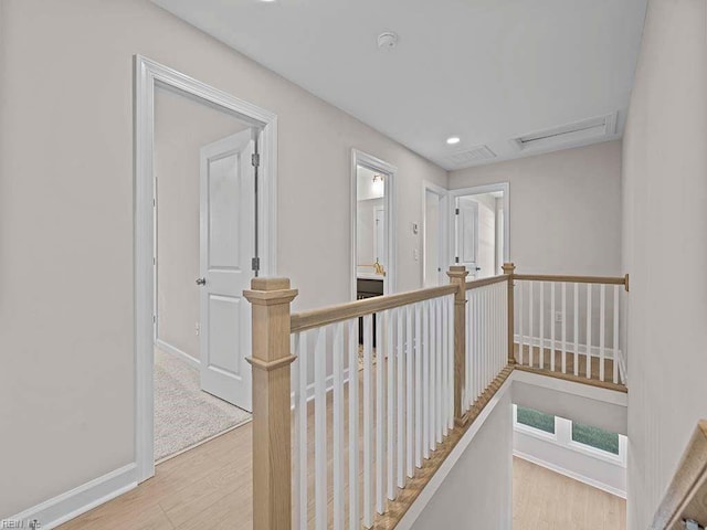 corridor featuring baseboards, visible vents, wood finished floors, and an upstairs landing